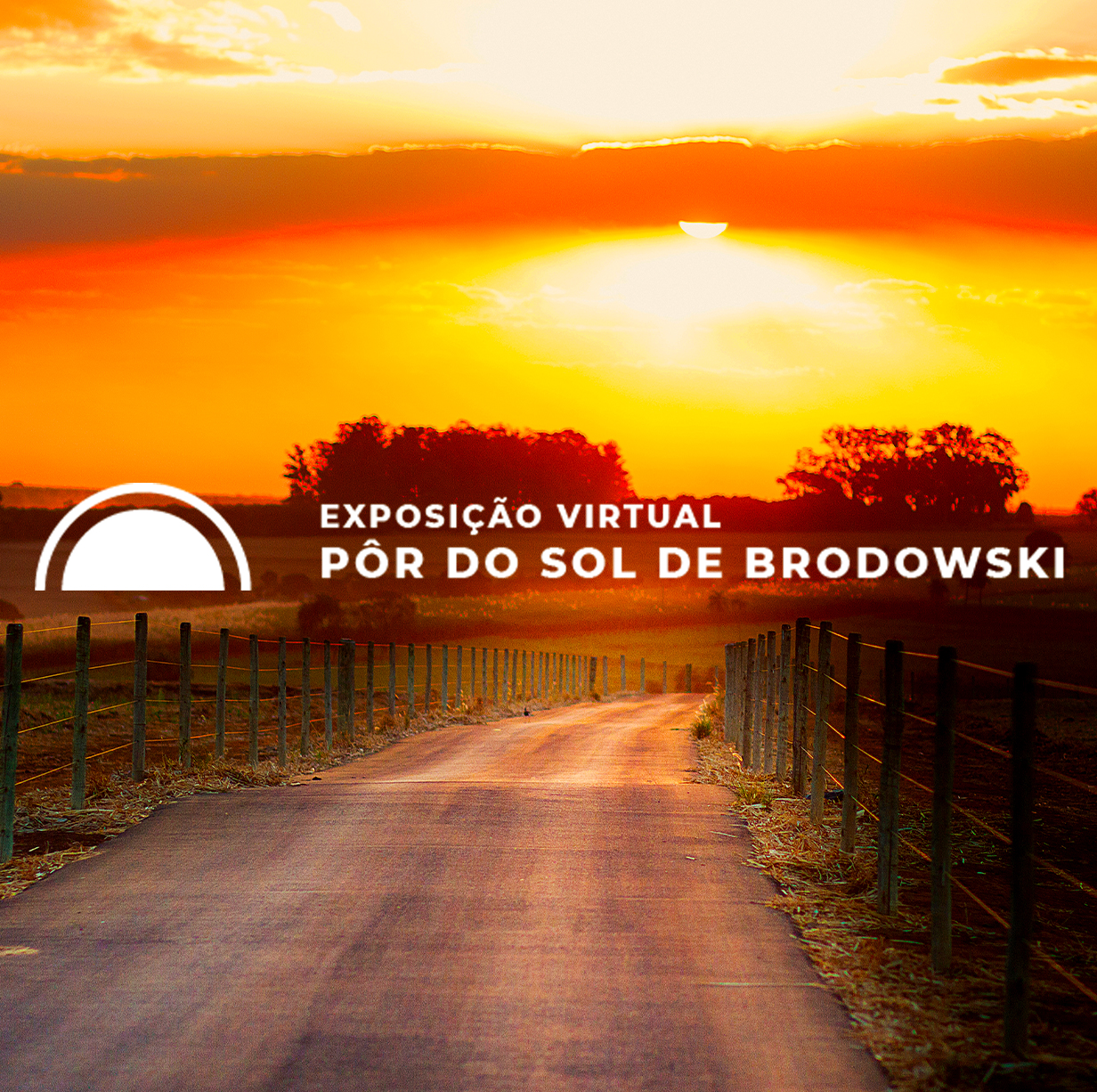 #PraCegoVer - Descrição da imagem para cegos: a imagem mostra uma das fotos da exposição. É um local descampado, com uma estrada de terra no meio e grama e árvores ao fundo. No céu está um pôr do sol com fortes tons de laranja.