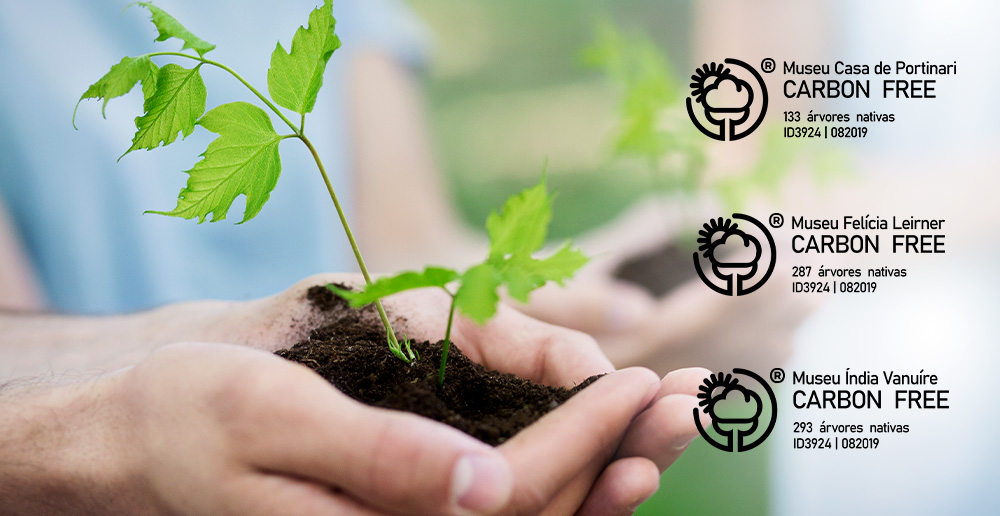 #PraCegoVer - Descrição da imagem para cegos: a arte mostra, ao fundo, uma mão segurando um punhado de terra com uma muda brotando. Na lateral direita, estão três selos, cada um de um museu, com o nome do local e a quantidade de árvores nativas.