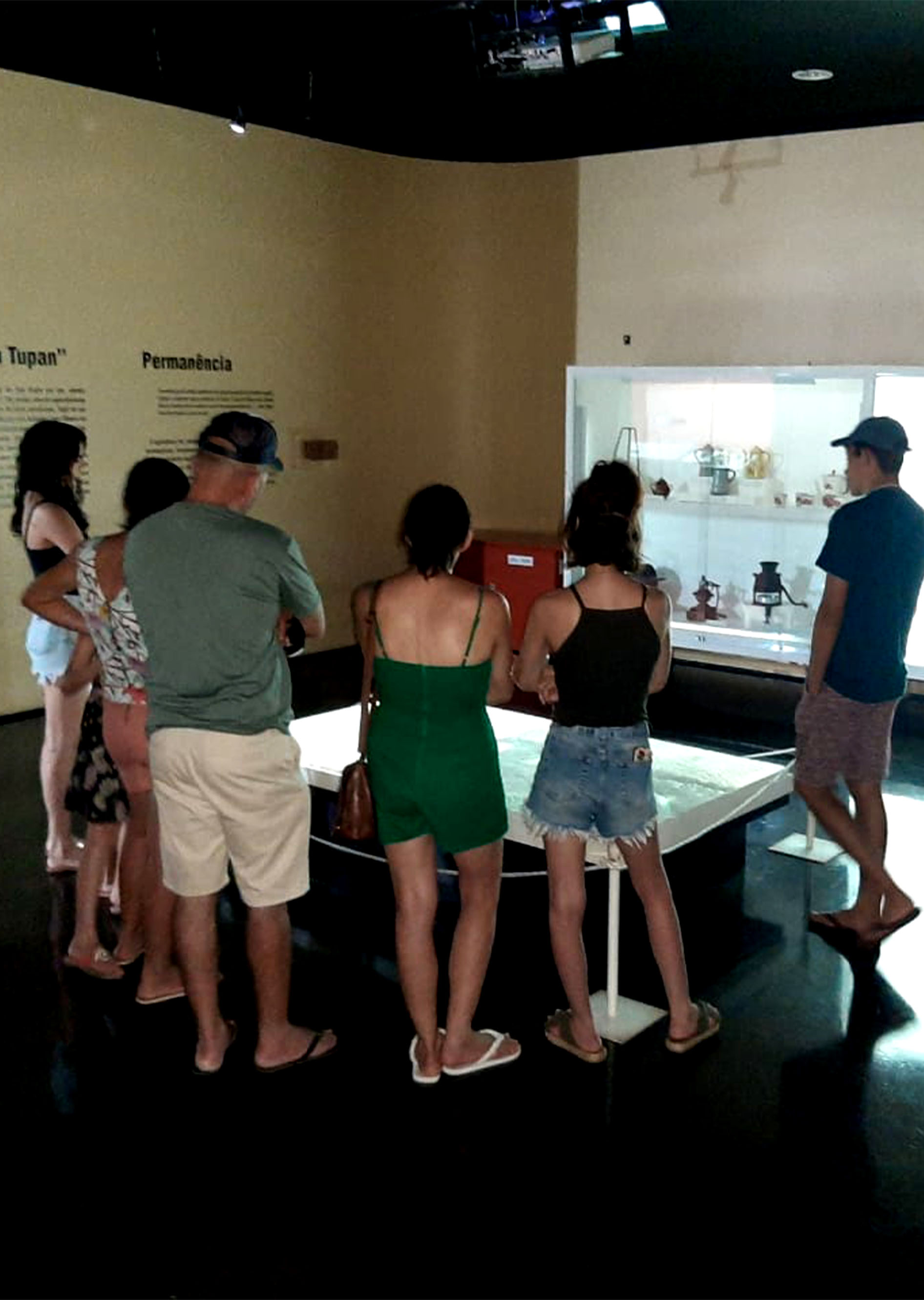 #PraCegoVer - Descrição da imagem para cegos: a foto mostra um grupo de pessoas numa das salas do Museu. Elas observam uma obra que está instalada no chão.