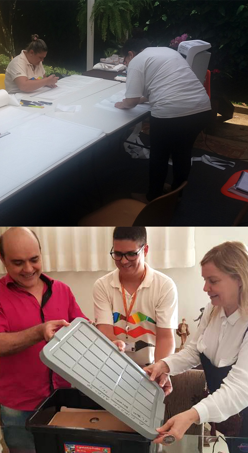 #PraCegoVer - Descrição da imagem para cegos: a primeira imagem mostra duas pessoas trabalhando ao redor de uma mesa branca. Uma está sentada e outra está em pé, e ambas estão mexendo em vários papéis. A segunda foto mostra três pessoas abrindo uma caixa de plástico preta e cinza, dentro dela aparecem alguns papéis e envelopes. Elas estão em uma sala, sorrindo e olhando para o objeto.

