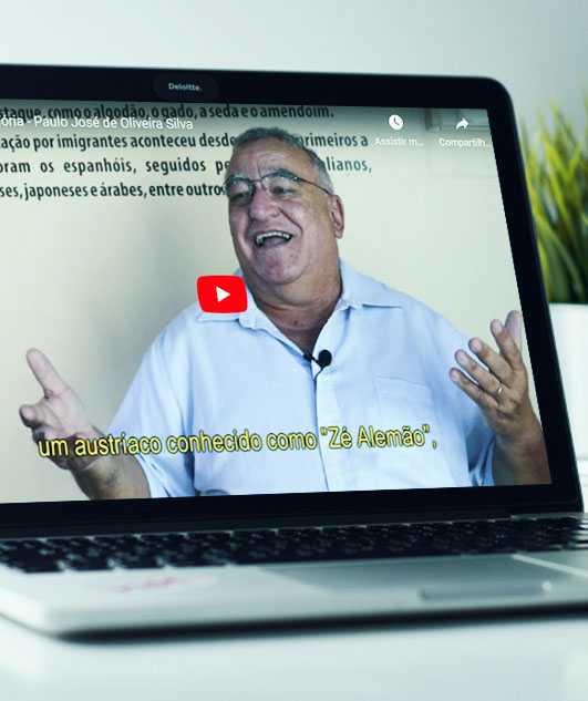 #PraCegoVer - Descrição da imagem para cegos: a imagem mostra um notebook aberto no vídeo que está na página do Museu. Nele aparece um homem sorrindo, de óculos e camisa branca, gesticulando com as mãos.