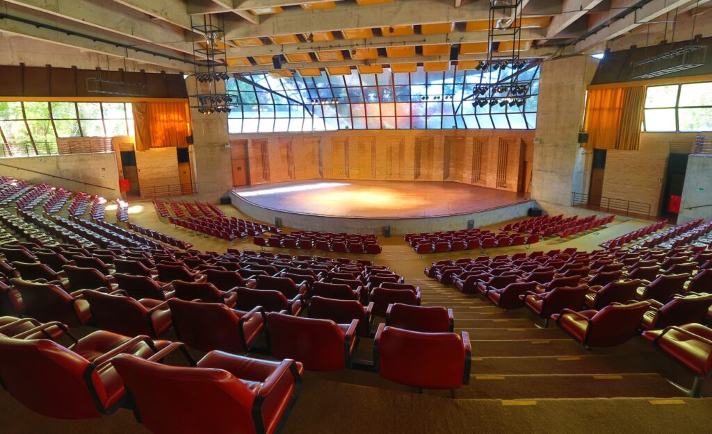 PraTodosVerem – A imagem mostra o palco do Auditório Claudio Santoro, exibindo cinco conjuntos com fileiras de cadeiras vermelhas e acolchoadas.