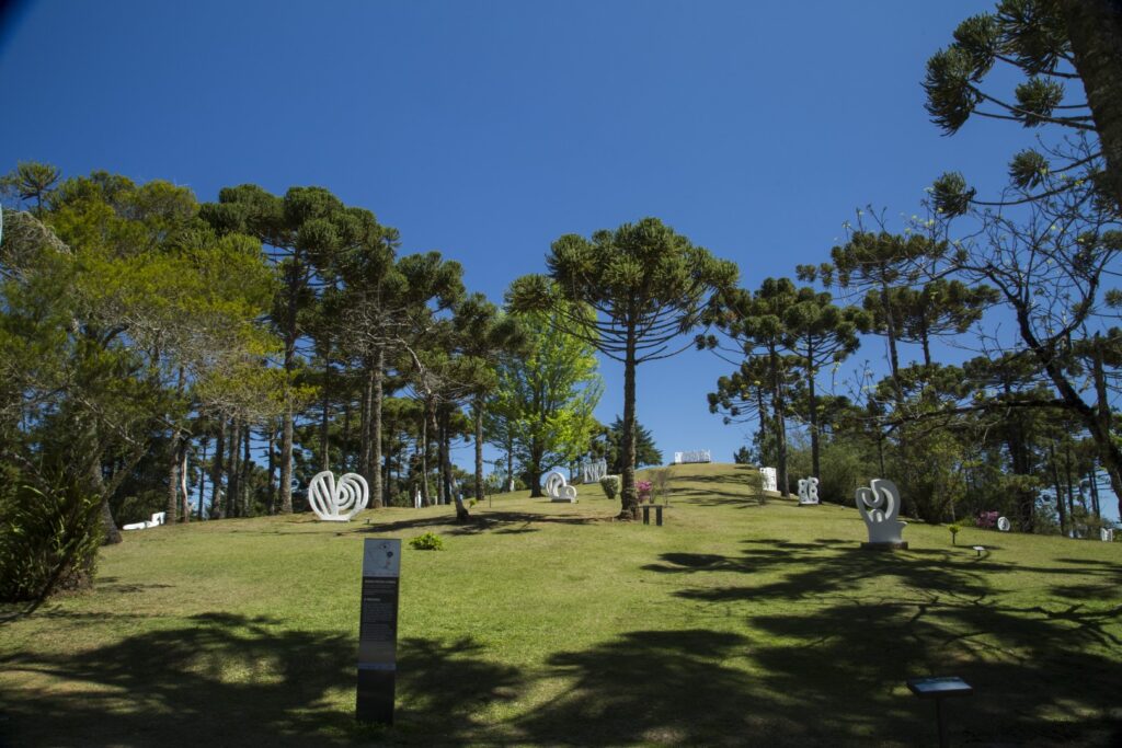 ParaTodosVerem: Imagem de um jardim gramado com muitas árvores e o céu azul. No chão, esculturas brancas em formatos geométricos. 
