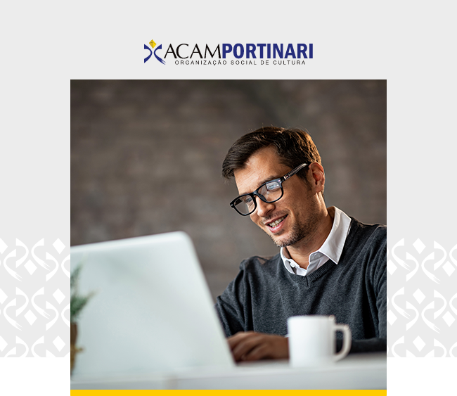 Na parte superior da imagem, o logotipo da ACAM Portinari aparece centralizado sobre um fundo cinza claro. Abaixo, em destaque, a fotografia de um homem de óculos e barba curta, sorrindo enquanto utiliza um notebook. Ele veste camisa branca e suéter cinza escuro. Em primeiro plano, à direita, uma caneca branca sobre a mesa. No canto inferior esquerdo, parte de uma planta aparece desfocada. Ao fundo, o ambiente tem parede em tom escuro e iluminação suave. Nas laterais da imagem, elementos gráficos brancos remetem à identidade visual da ACAM Portinari.