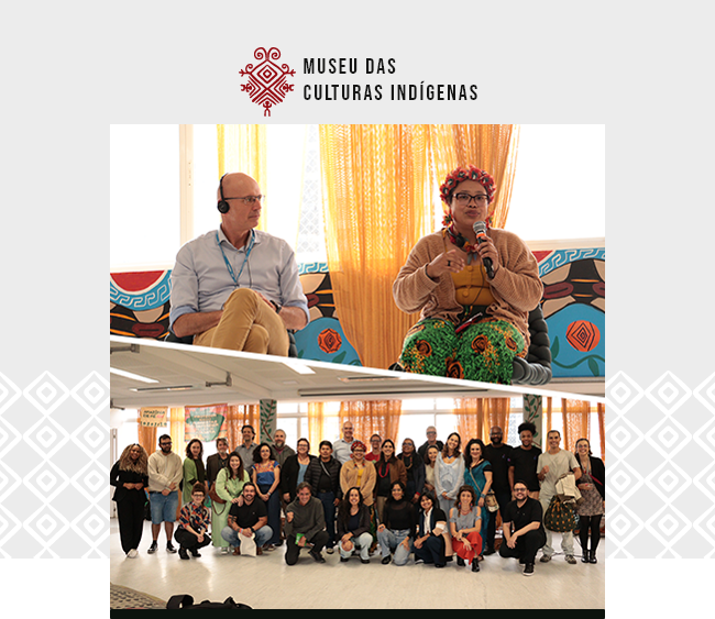 Imagem com o logotipo do Museu das Culturas Indígenas centralizado na parte superior, sobre fundo claro. Abaixo, duas fotografias compõem a imagem. Na parte superior, duas pessoas estão sentadas em um espaço interno. À esquerda, um homem usa fones de ouvido e observa a interlocutora. À direita, uma mulher indígena, com adorno floral na cabeça e vestimenta estampada, segura um microfone e fala ao público, sentada diante de um fundo com tecidos e grafismos coloridos. Na parte inferior, uma fotografia de grupo mostra dezenas de pessoas reunidas em um espaço amplo e iluminado, posando para a câmera após a atividade. Elementos gráficos da identidade visual do Museu das Culturas Indígenas aparecem nas laterais da imagem, com uma faixa vermelha na base.
