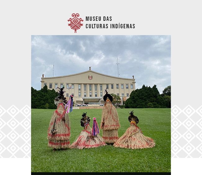 Arte em fundo cinza claro e branco. Acima, logomarca do Museu das Culturas Indígenas. No centro, uma foto de quatro pessoas, duas em pé e duas sentadas, com vestes rituais características da etnia indígena Pankararu, que consistem em mantos de fibras naturais beges com alguns grafismos vermelhos que cobrem o corpo todo. Estão em um grande gramado com um palácio ao fundo. No palácio de vários andares, é possível ver o brasão do Estado de São Paulo ao centro.