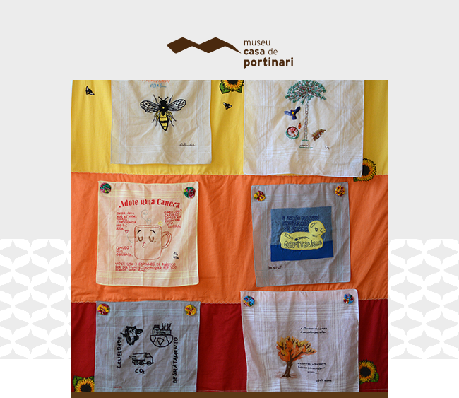 Imagem com o logotipo do Museu Casa de Portinari centralizado na parte superior, sobre fundo claro. Abaixo, um painel artesanal formado por lenços coloridos costurados sobre faixas de tecido nas cores amarelo, laranja e vermelho. Cada lenço apresenta bordados ou pinturas com desenhos, frases e mensagens educativas, incluindo elementos como abelhas, árvores, canecas, animais e símbolos de reciclagem. Detalhes de girassóis decoram os cantos do painel. Elementos gráficos da identidade visual do museu aparecem nas laterais da imagem.