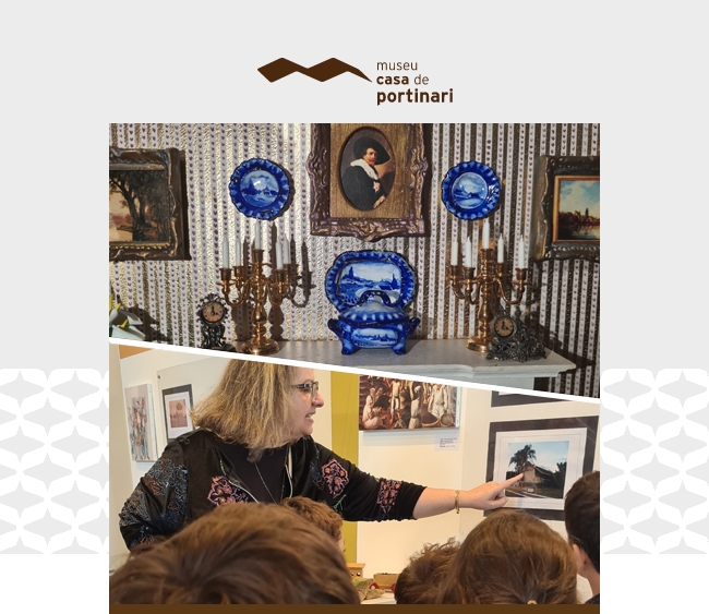 Imagem com o logotipo do Museu Casa de Portinari centralizado na parte superior, sobre fundo claro com padrões gráficos discretos nas laterais. Abaixo, duas fotografias são dispostas em diagonal, formando um recorte dinâmico. Na parte superior, vê-se uma composição miniaturizada com pratos e peças decorativas em tom de azul sobre uma mesa, ladeadas por castiçais e relógios antigos, com pinturas emolduradas ao fundo. Na parte inferior, uma educadora conduz um grupo de visitantes; ela aponta para uma obra exposta na parede enquanto dialoga com as crianças à sua frente, que estão de costas para o observador.
