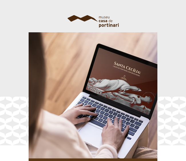 Imagem com o logotipo do Museu Casa de Portinari centralizado na parte superior, sobre fundo claro. Abaixo, uma fotografia em destaque mostra uma pessoa sentada, vista por trás, utilizando um notebook apoiado sobre o colo. As mãos estão posicionadas sobre o teclado, indicando interação com o computador. Na tela do notebook, aparece a capa digital do conteúdo “Santa Cecília”, com a reprodução de uma escultura representando uma mulher deitada, acompanhada de texto informativo. O ambiente sugere um espaço interno, com piso de madeira ao fundo, desfocado. Elementos gráficos da identidade visual do Museu Casa de Portinari aparecem nas laterais da imagem, com uma faixa cinza na base.
