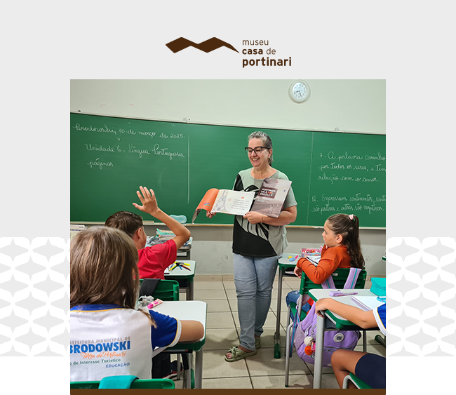 Na parte superior da imagem, sobre fundo claro, aparece o logotipo do Museu Casa de Portinari. Ao centro da composição, uma fotografia mostra uma sala de aula. Uma educadora está em pé entre as carteiras, sorrindo, enquanto segura um livro aberto nas mãos e apresenta o conteúdo aos estudantes. Ela usa óculos e veste camiseta em tons claros com detalhes escuros. Ao redor, crianças sentadas em carteiras escolares acompanham a atividade. Uma delas levanta a mão para participar, enquanto outra observa atentamente a professora. No fundo da sala, um quadro verde ocupa toda a parede, com anotações escritas em giz branco e um relógio fixado acima. Sobre as mesas há cadernos, lápis, estojos e outros materiais escolares. Nas laterais da composição aparecem padrões gráficos discretos que dialogam com a identidade visual da instituição.