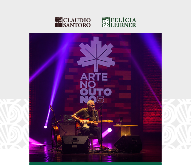Na parte superior da imagem, sobre fundo cinza claro, aparecem os logotipos do Auditório Claudio Santoro e do Museu Felícia Leirner. Ao centro, há uma fotografia em formato retangular. A imagem mostra uma mulher de cabelos curtos sentada no palco. Ela toca uma guitarra elétrica e canta diante de um microfone. Ao seu redor, aparecem equipamentos de som, amplificadores, caixas acústicas, pedais e uma pequena mesa. Ao fundo, destaca-se o painel do festival Arte no Outono, com o logotipo em formato de folha e o texto “ARTE NO OUTONO Nº 5” em letras claras sobre uma composição de tons avermelhados. Feixes de luz roxa iluminam o palco e atravessam a cena em diferentes direções. As laterais do palco apresentam paredes de tijolos aparentes iluminadas em vermelho. Nas laterais da composição, sobre o fundo cinza, há padrões gráficos em tom branco. Na parte inferior da fotografia, uma faixa verde acompanha a base da imagem.