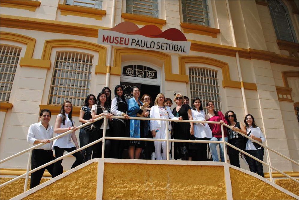 PraTodosVerem – A imagem mostra dezesseis mulheres enfileiradas na escadaria em frente ao Museu Paulo Setúbal. As paredes da instituição possuem detalhes bege e amarelo. 